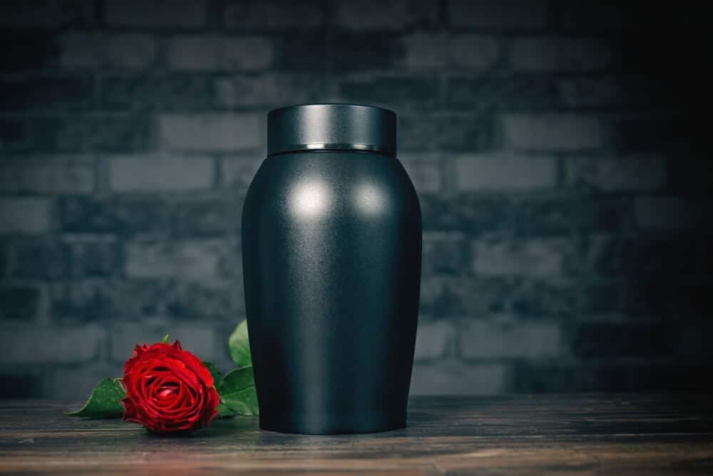Black cremation urn with a red rose on a wooden table.