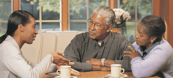 Grown daughter sitting at a table talking with elderly parents