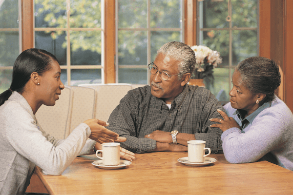 Grown daughter sitting at a table talking with elderly parents