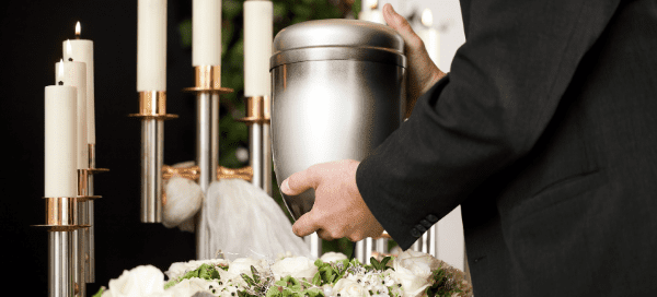 Hands placing urn on bed of flowers in front of lit candles