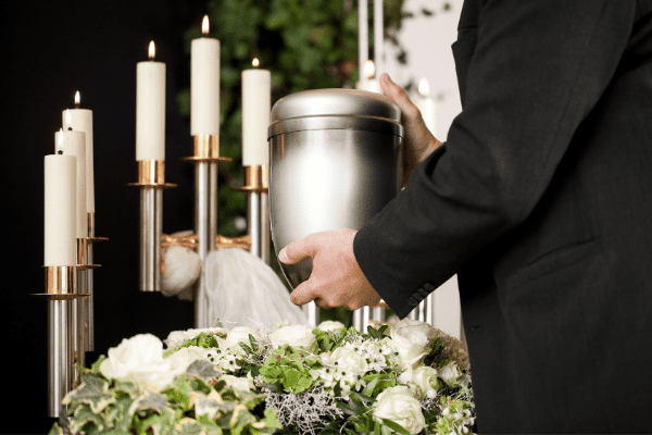 Hands placing urn on bed of flowers in front of lit candles