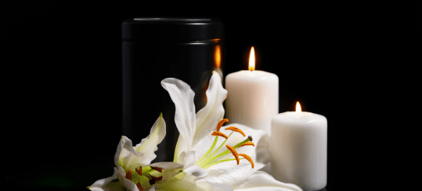 Black urn against a black background with white flowers and candles