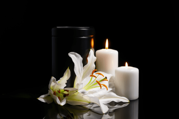 Black urn against a black background with white flowers and candles