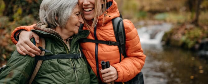 A daughter and her mother hugging while they are going on a hike in the woods together.